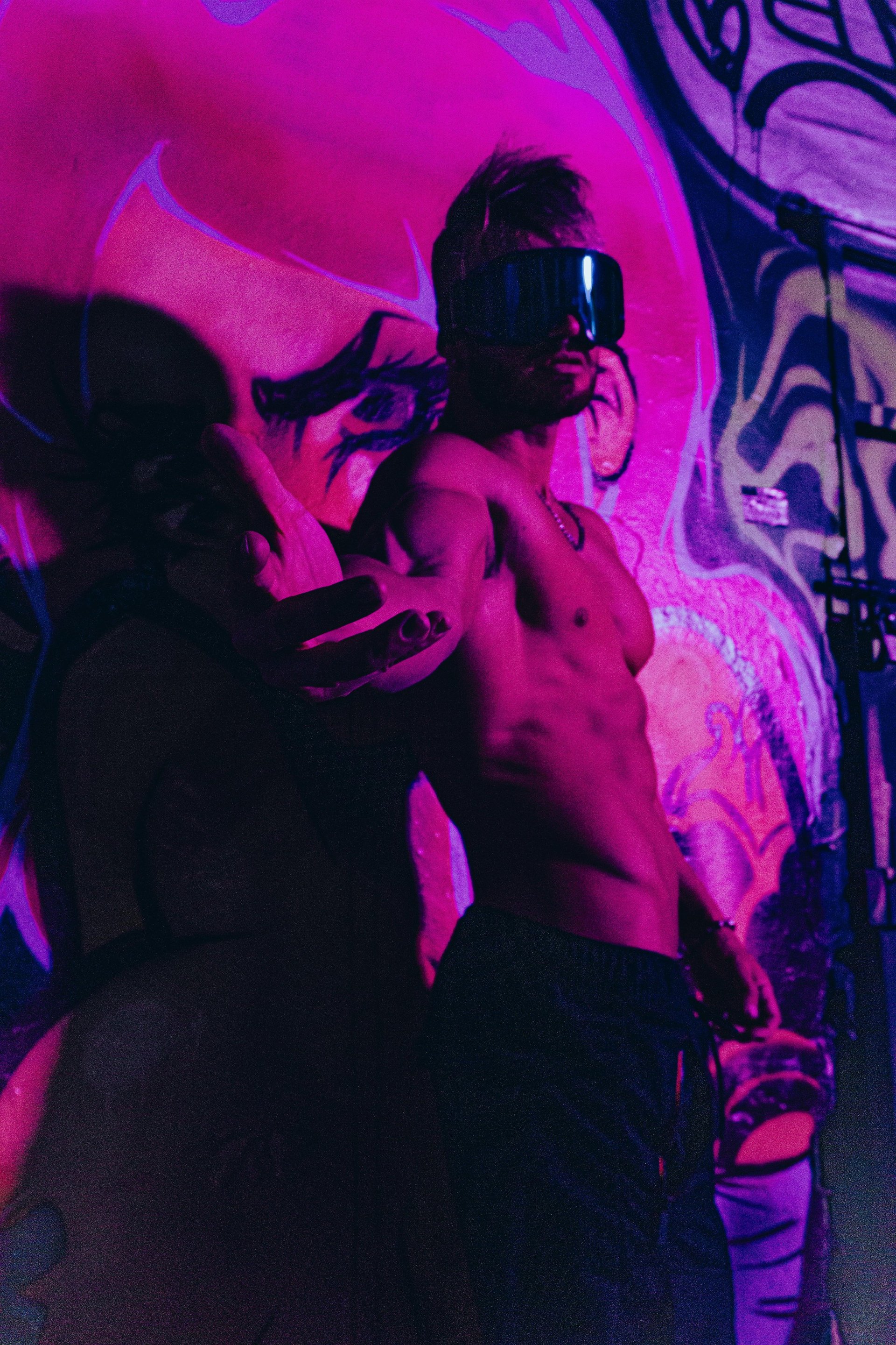Two shirtless people wearing VR headsets in neon pink and blue lighting