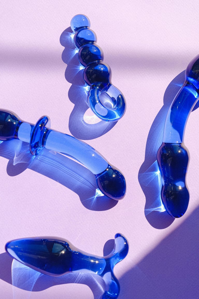 Blue glass sculptural objects with bubble and abstract shapes arranged on a pink background with dramatic shadows