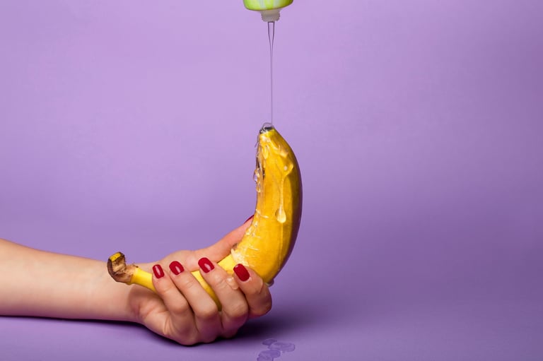 Hand holding a banana with red nail polish against a purple background with liquid dripping from above