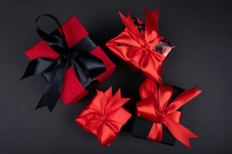 Three wrapped red and black gift boxes with bows arranged on a dark gray background